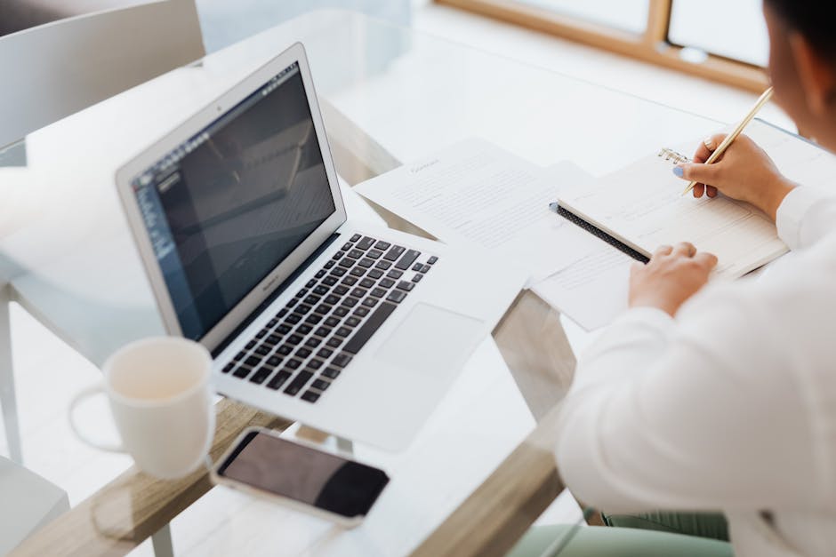 person writing on laptop surrounded by technology