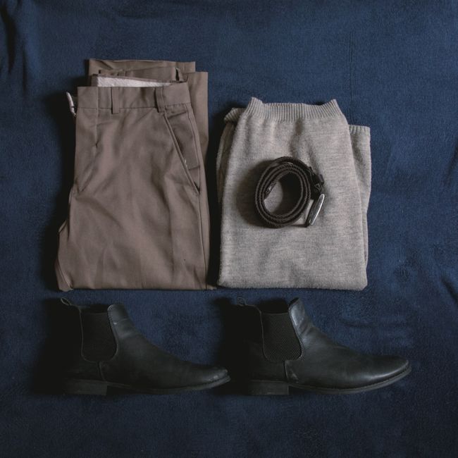 Overhead shot of a meticulously arranged capsule travel wardrobe featuring neutral tops, pants, a dress, and accessories.