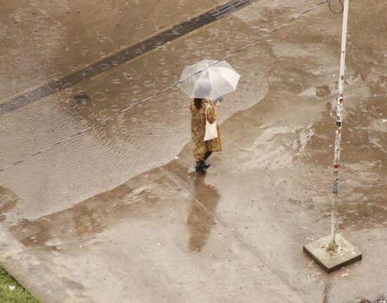 Person walking on a wet city street, wearing waterproof shoes and holding an umbrella.