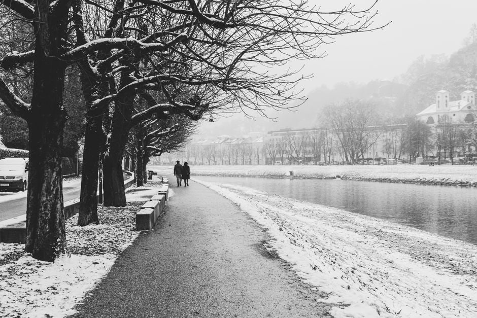 Couple in warm clothing walking along a snowy street with historic buildings in a European city.