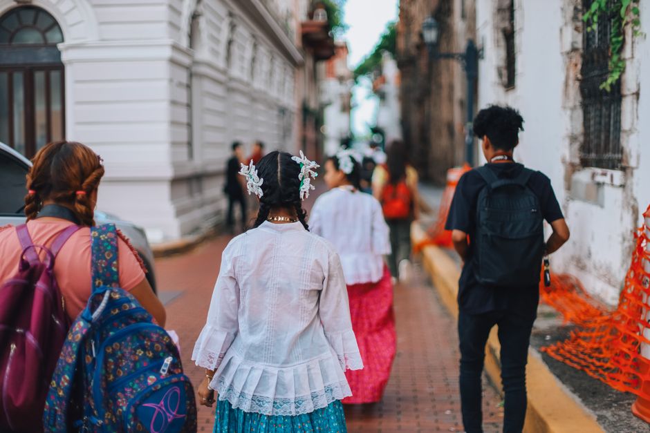 People walking through a sunny, humid city street, with blurred city buildings in the background, conveying summer heat.