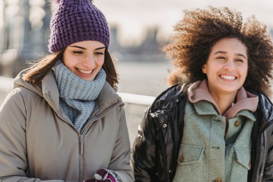 A group of diverse women laughing and walking together in a bustling cold city, dressed in various stylish and warm layered winter outfits suitable for urban exploration.