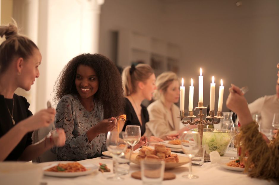A group of women, dressed in stylish and varied outfits, enjoying a lively dinner party at a well-lit restaurant.