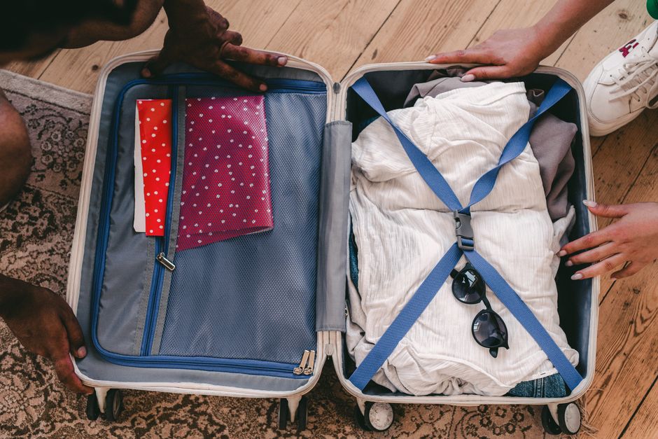 Open fabric travel bag on a bed, neatly organized with clothes, a laptop, and small personal items, showcasing internal compartments.