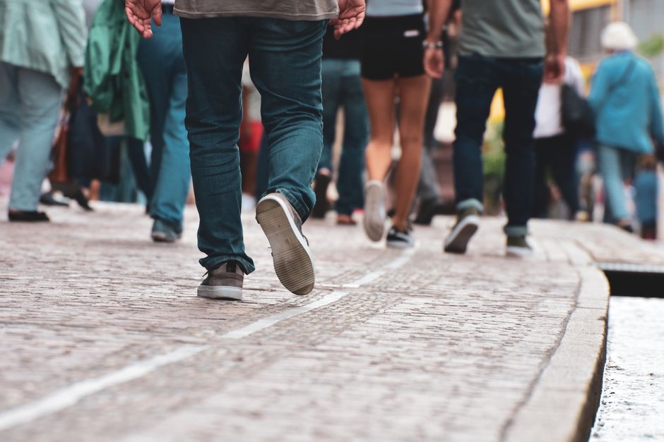A close-up of a person's feet, wearing supportive walking shoes, stepping on uneven, historic cobblestones in an old European city, emphasizing durability and comfort.