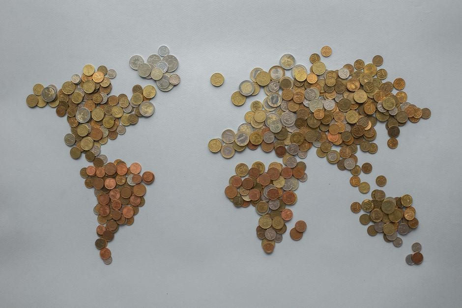 A stylized world map overlays various currency symbols and small shopping bags, representing international online shopping and the consideration of global deals and offers across different regions like the US and Europe.