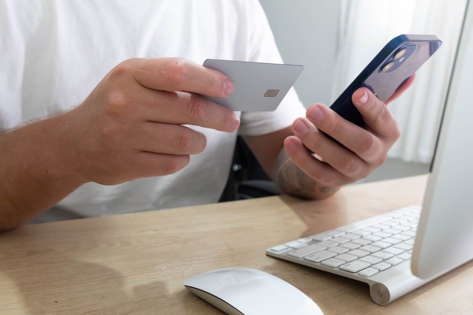 Hands holding a smartphone displaying an online store and a credit card, illustrating the final steps of a smart online purchase after verifying a deal.