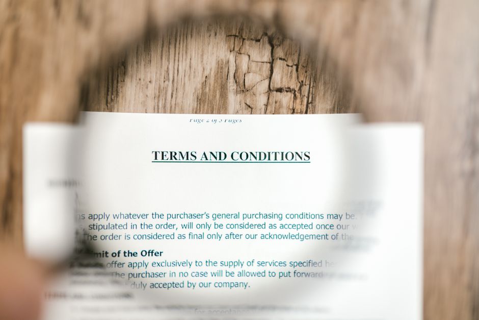A magnifying glass hovering over dense, small print on a digital document, symbolizing the need to scrutinize terms and conditions carefully.