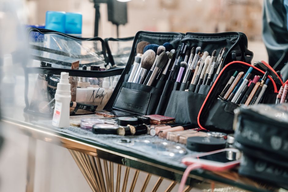 An open makeup bag on a wooden table, filled with various affordable beauty products such as a BB cream, mascara, lip balm, and a small brush, showcasing accessible makeup options.