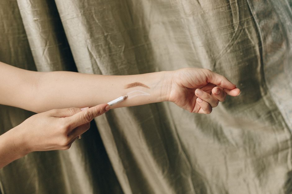 Multiple shades of liquid foundation swatched on a forearm, demonstrating different undertones from cool to warm.