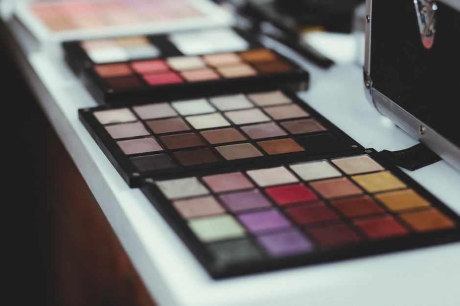 A close-up of a diverse makeup palette featuring various shades of eyeshadows, blushes, and lip colors, organized by warm and cool tones, as advised by a practical beauty and skincare guide.