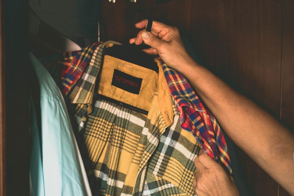 A focused man selecting a button-down shirt from a thoughtfully organized closet, representing a men's capsule wardrobe.