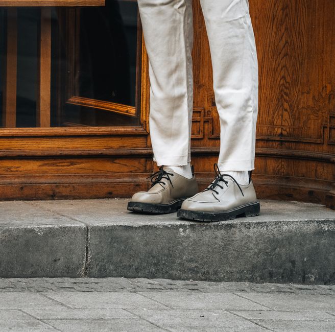 A stylish man wearing a smart casual neutral outfit, walking confidently through a historic European city street.