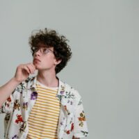A man in a simple, neutral-colored sustainable outfit, looking contemplatively at his clothing choices, symbolizing thoughtful fashion decisions.
