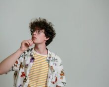 A man in a simple, neutral-colored sustainable outfit, looking contemplatively at his clothing choices, symbolizing thoughtful fashion decisions.