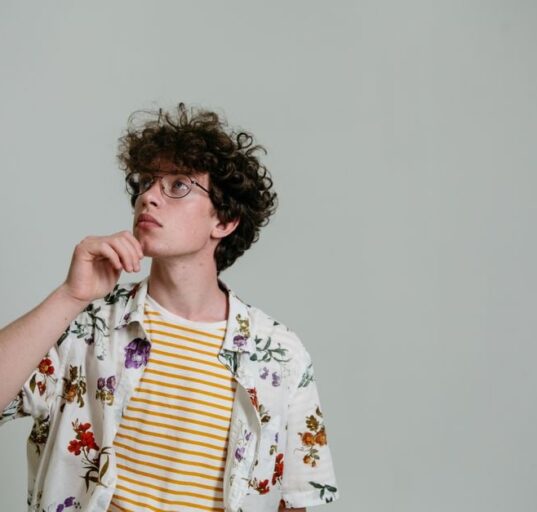 A man in a simple, neutral-colored sustainable outfit, looking contemplatively at his clothing choices, symbolizing thoughtful fashion decisions.