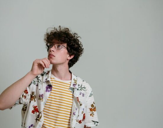 A man in a simple, neutral-colored sustainable outfit, looking contemplatively at his clothing choices, symbolizing thoughtful fashion decisions.