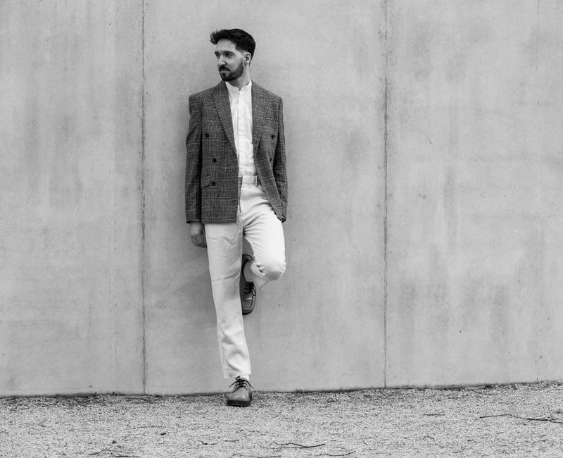 A man dressed in a versatile smart casual outfit, featuring a navy blazer, light blue shirt, chinos, and white sneakers, suitable for urban settings like Paris or London.