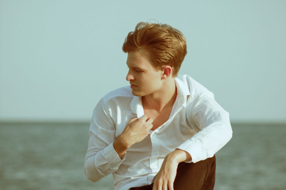 A man wearing a white linen shirt and lightweight light-colored chinos stands by a body of water, illustrating practical and stylish men's summer outfits for hot weather.