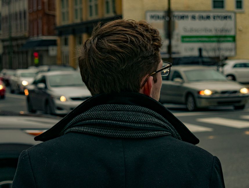 Stylish man in a well-fitted wool overcoat and cashmere scarf, standing on a bustling city street, illustrating practical winter menswear essentials.