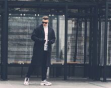 A man in a city setting, demonstrating effective winter layering with a wool overcoat, scarf, and gloves.