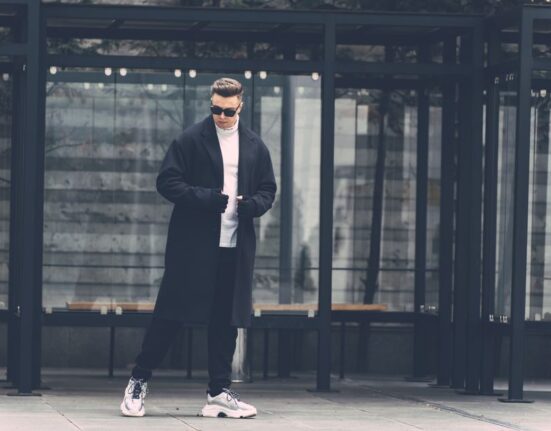 A man in a city setting, demonstrating effective winter layering with a wool overcoat, scarf, and gloves.