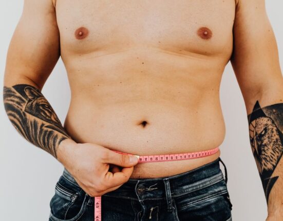 A man meticulously measuring the waist of a pair of jeans with a fabric tape measure, emphasizing the importance of accurate sizing for online purchases.
