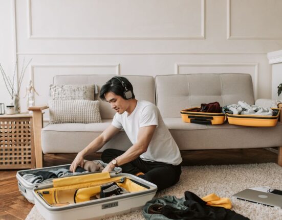 A man carefully folding versatile clothes into a minimalist suitcase, demonstrating efficient packing for a trip.