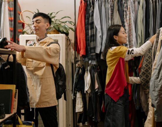 Man thoughtfully browsing hangers of clothing in a minimalist, light-filled sustainable fashion boutique.