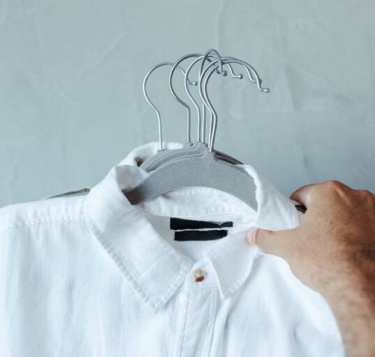 A man in a modern, organized closet carefully selecting a shirt, demonstrating the principle of a minimalist wardrobe.
