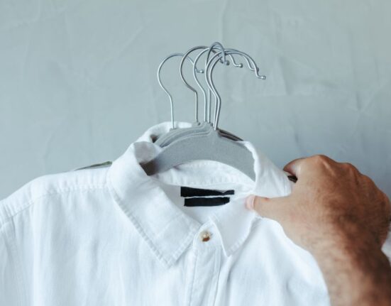 A man in a modern, organized closet carefully selecting a shirt, demonstrating the principle of a minimalist wardrobe.