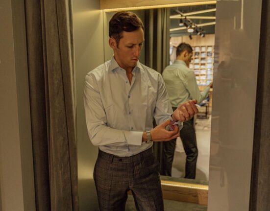 Man examining a lightweight linen shirt in a clothing store, illustrating fabric choice for men's summer outfits for hot weather.