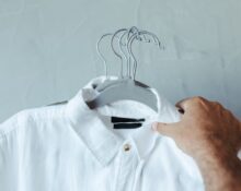 A man in a bright, naturally lit room, trying on a light-colored, sustainably made organic cotton shirt, checking the fit in a mirror.