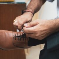 A man in a navy suit sitting down, adjusting the laces of his brown leather derby shoes, symbolizing the start of a comfortable workday.
