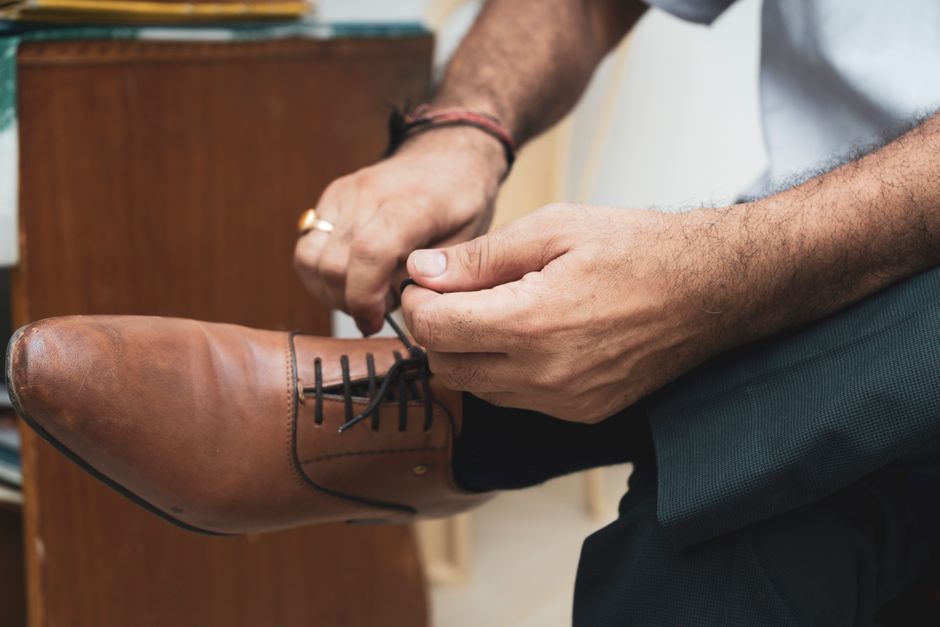 A man in tailored trousers and polished leather shoes, bending to tie his laces, showing attention to detail before an evening out.