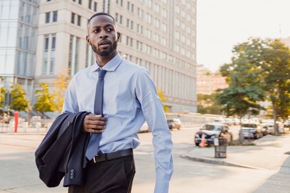 A man in a breathable, light brown linen blazer and trousers walks through a European city square, showcasing a smart casual men's summer outfit perfect for hot weather.
