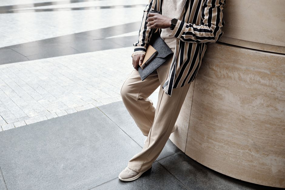 Close-up of a man's smart casual outfit: neutral chinos, white sneakers, and a light blue oxford shirt, showing attention to detail.