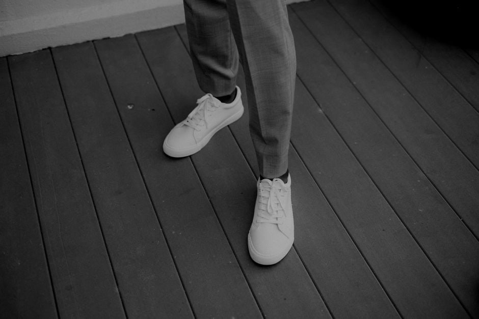 Close-up of a man's feet wearing sleek, white leather dress sneakers with tailored navy blue trousers, illustrating a smart casual outfit.