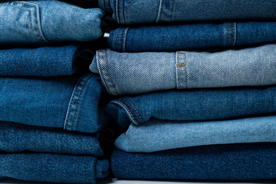 A well-organized men's wardrobe with neatly folded jeans in different fits and washes, alongside other clothing items, emphasizing a capsule wardrobe approach.