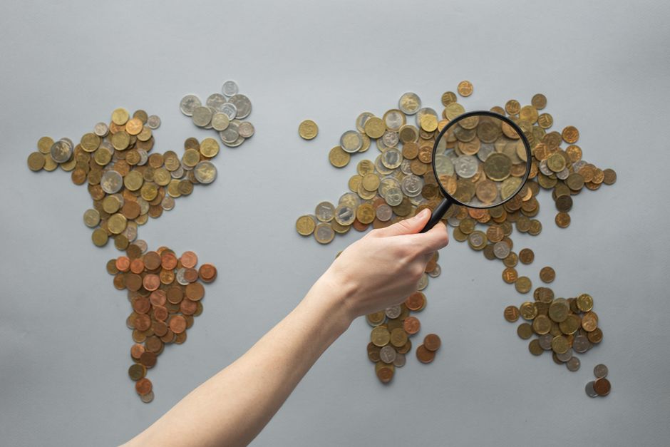 A shopping cart surrounded by different currency symbols on a world map background, representing international deal comparison.