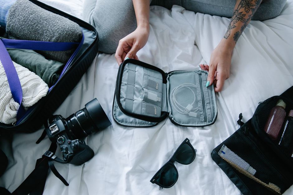 An open grey travel backpack showcasing multiple compartments, including a padded laptop sleeve, mesh pockets, and compression straps with neatly packed clothes.