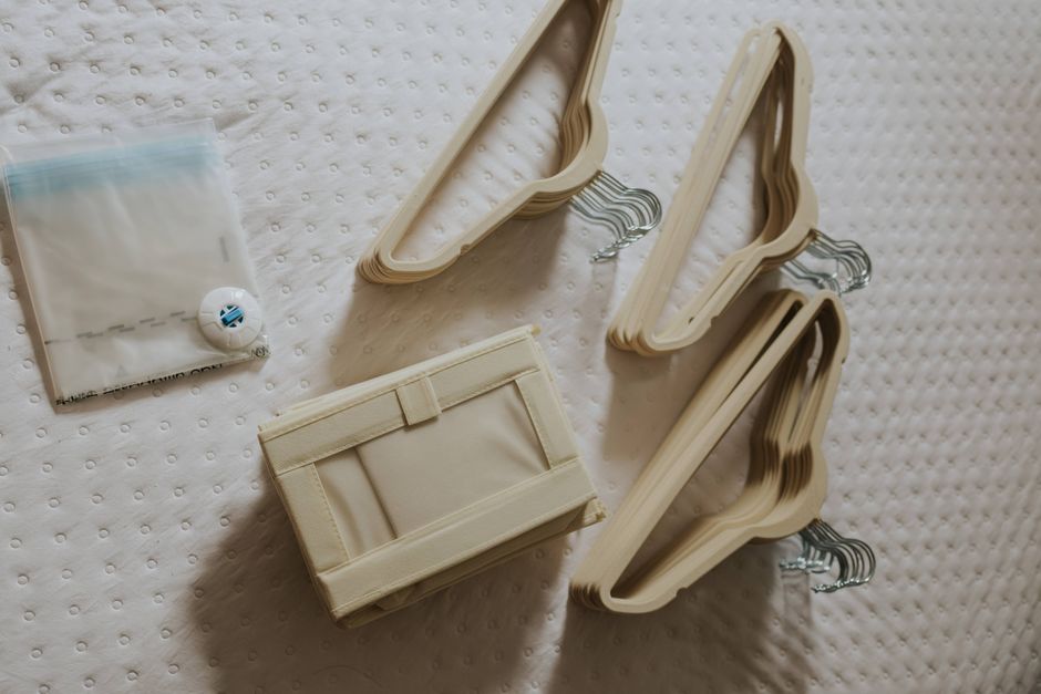 An overhead view of a perfectly organized capsule travel wardrobe laid out on a bed, featuring neutral tops, versatile bottoms, a trench coat, and two pairs of shoes.