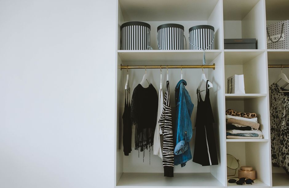 A neatly organized minimalist closet with a range of neutral-toned clothing items (blouses, trousers, sweaters) hanging uniformly, illustrating a clean capsule wardrobe.