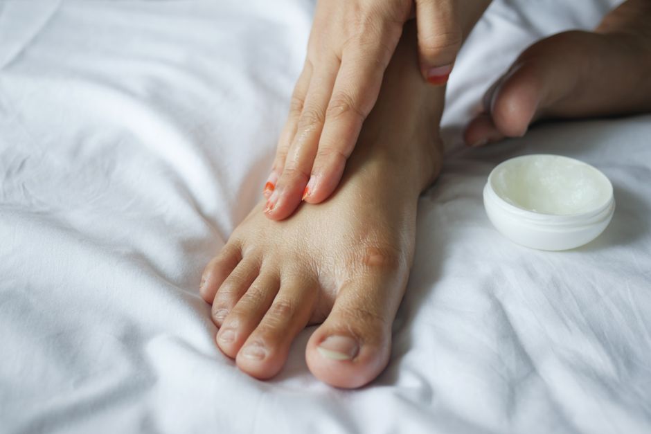 A close-up shot of a hand applying an anti-blister balm to the heel of a foot before putting on new shoes.