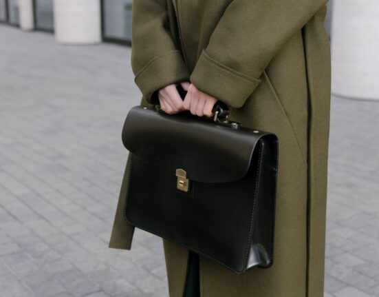 Close-up of a hand gently cleaning a brown leather briefcase with a soft cloth and leather cleaner.