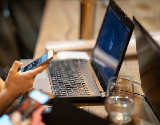 A person comparing online deals on a laptop and smartphone, illustrating the challenge of finding the best prices across platforms.