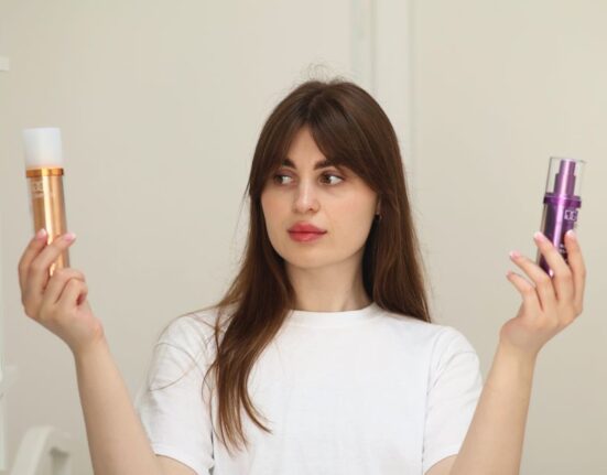 A person's hands holding up two different beauty product bottles, comparing their ingredient lists with a confused expression.