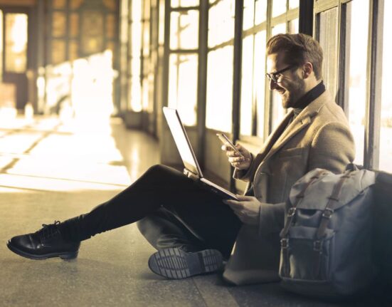 A person comparing flight and hotel deals on a laptop and smartphone, surrounded by travel items.