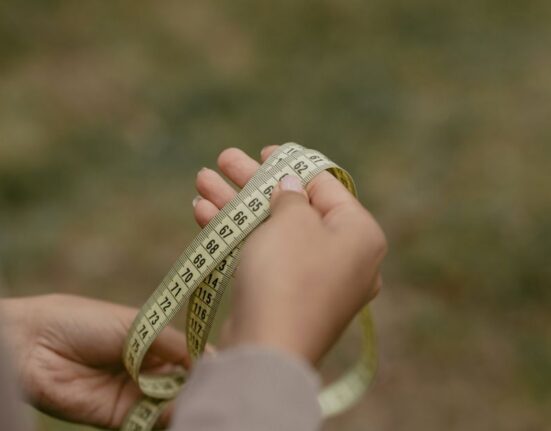 A person accurately measuring their foot length and width on a piece of paper with a ruler, preparing for online shoe shopping.