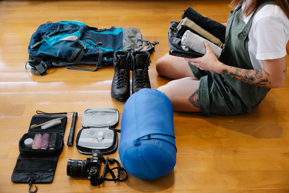 Overhead shot of an open travel backpack showing a laptop, notebook, water bottle, and charger neatly organized in various compartments.